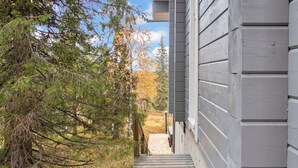 A pathway leading to a building with grey siding, surrounded by trees and shrubs. - Vuosseli-kelkka 15a by Interhome (Kuusamo)