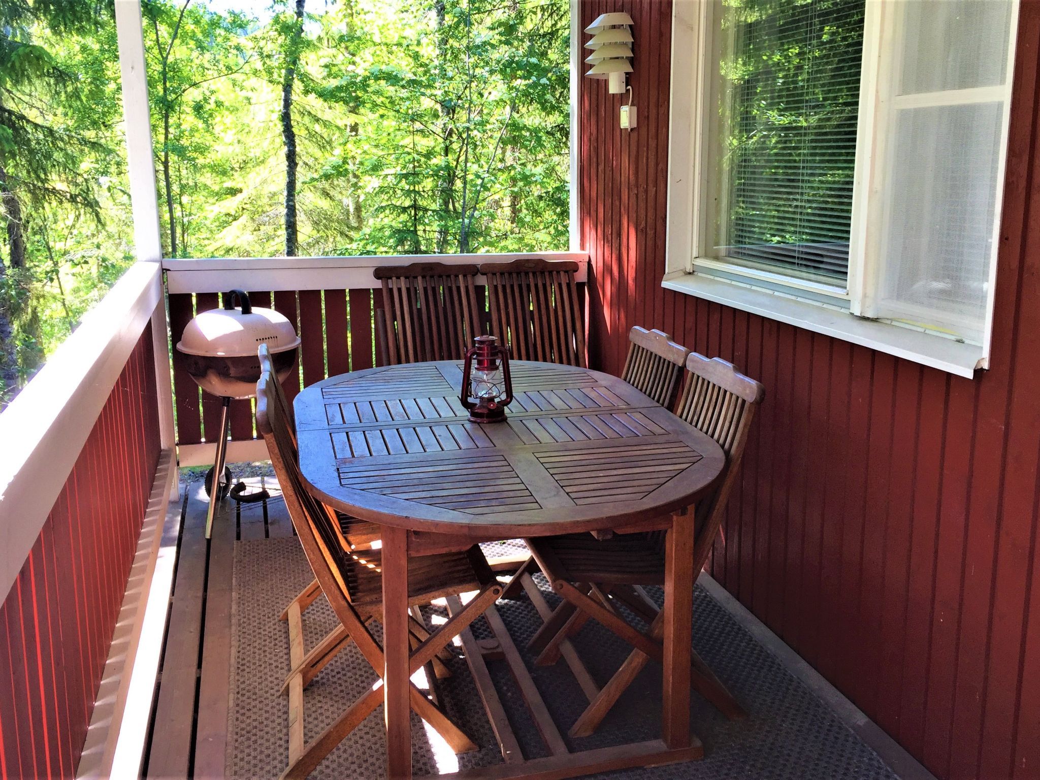 Une terrasse en bois avec une table ronde et des chaises, un barbecue et une lanterne.