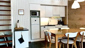 A compact kitchen with a refrigerator, microwave, and stove. There is a dining table with chairs and a hanging coat rack. - Weekend family by Interhome (Sotkamo)