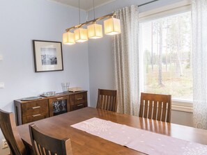 Et spiseområde med et træbord, stole, en lysekrone, et indrammet billede og et vindue med gardiner.