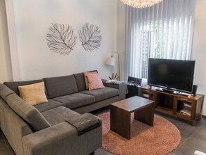 Una sala de estar moderna con un sofá gris, una mesa de centro, un televisor de pantalla plana sobre un soporte de madera y decoración en la pared.