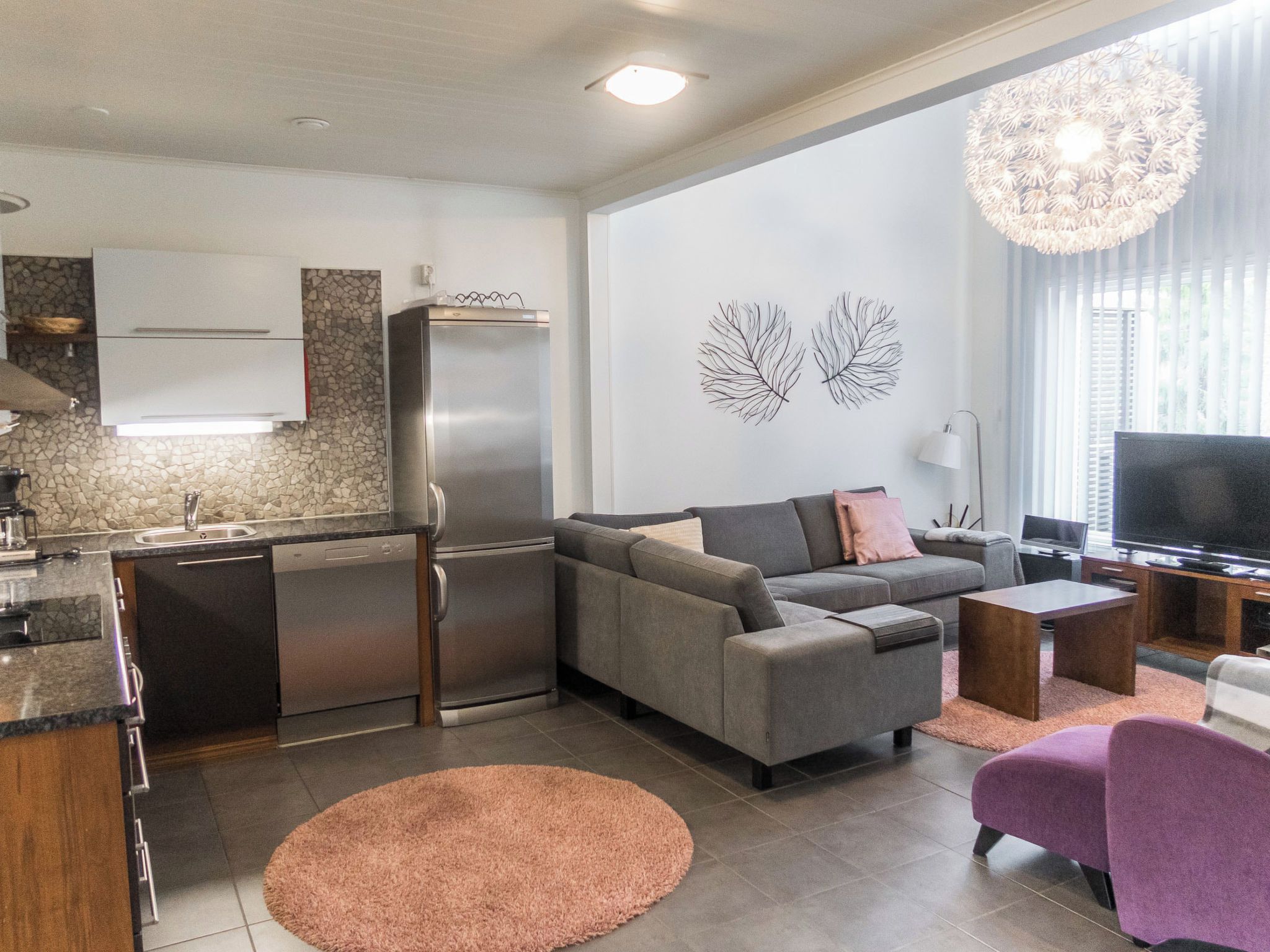 A modern living space with a kitchen, grey sofa, TV, and a decorative wall piece.