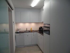 Una cocina compacta con armarios blancos, encimera negra y horno empotrado.