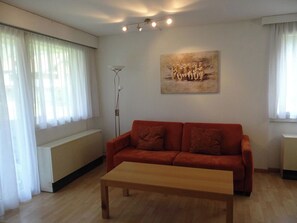 Una sala de estar con un sofá rojo, una mesa de centro de madera, una lámpara de pie y un cuadro en la pared.