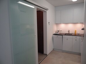 Une cuisine moderne avec des meubles blancs, un plan de travail noir et une porte visible donnant sur une autre pièce.