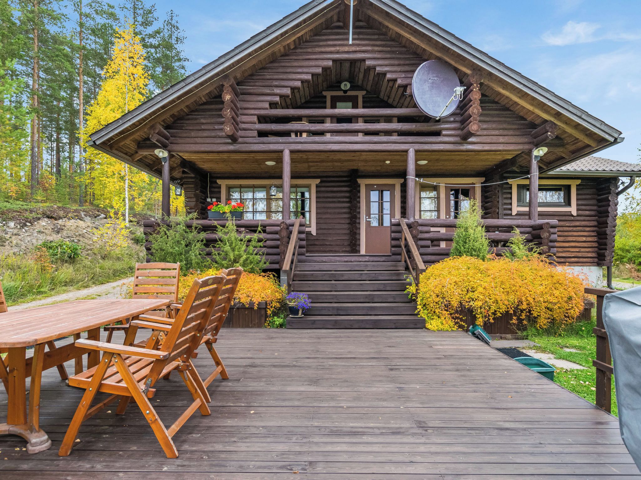 Une cabane en rondins dotée d’un porche, d’une terrasse en bois et d’un espace extérieur aménagé pour s’asseoir.