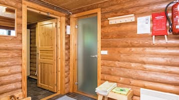 Ein Holzhütten-Interieur mit Holztür, einem kleinen Tisch mit einer Zeitschrift, einem Feuerlöscher und einem Thermostat an der Wand.