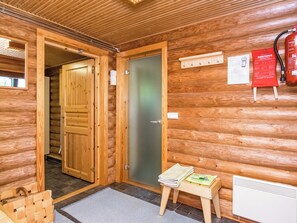 Ein Holzhütten-Interieur mit Holztür, einem kleinen Tisch mit einer Zeitschrift, einem Feuerlöscher und einem Thermostat an der Wand.