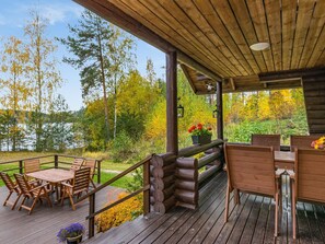 A wooden deck with a table and chairs, overlooking a lake and autumn foliage.