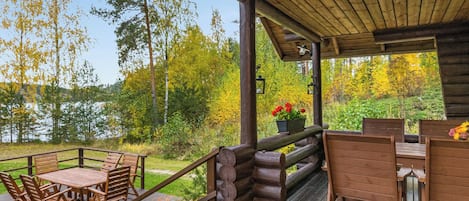 Um deck de madeira com mesa e cadeiras, cercado por um corrimão, com vista para um lago e floresta.
