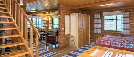 L'intérieur d'une cabane en rondins, avec un escalier en bois, une cheminée, un canapé, un lit et une fenêtre avec des rideaux.