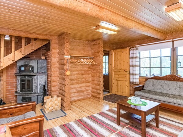 A log cabin interior with a fireplace, wooden furniture, and a large window.