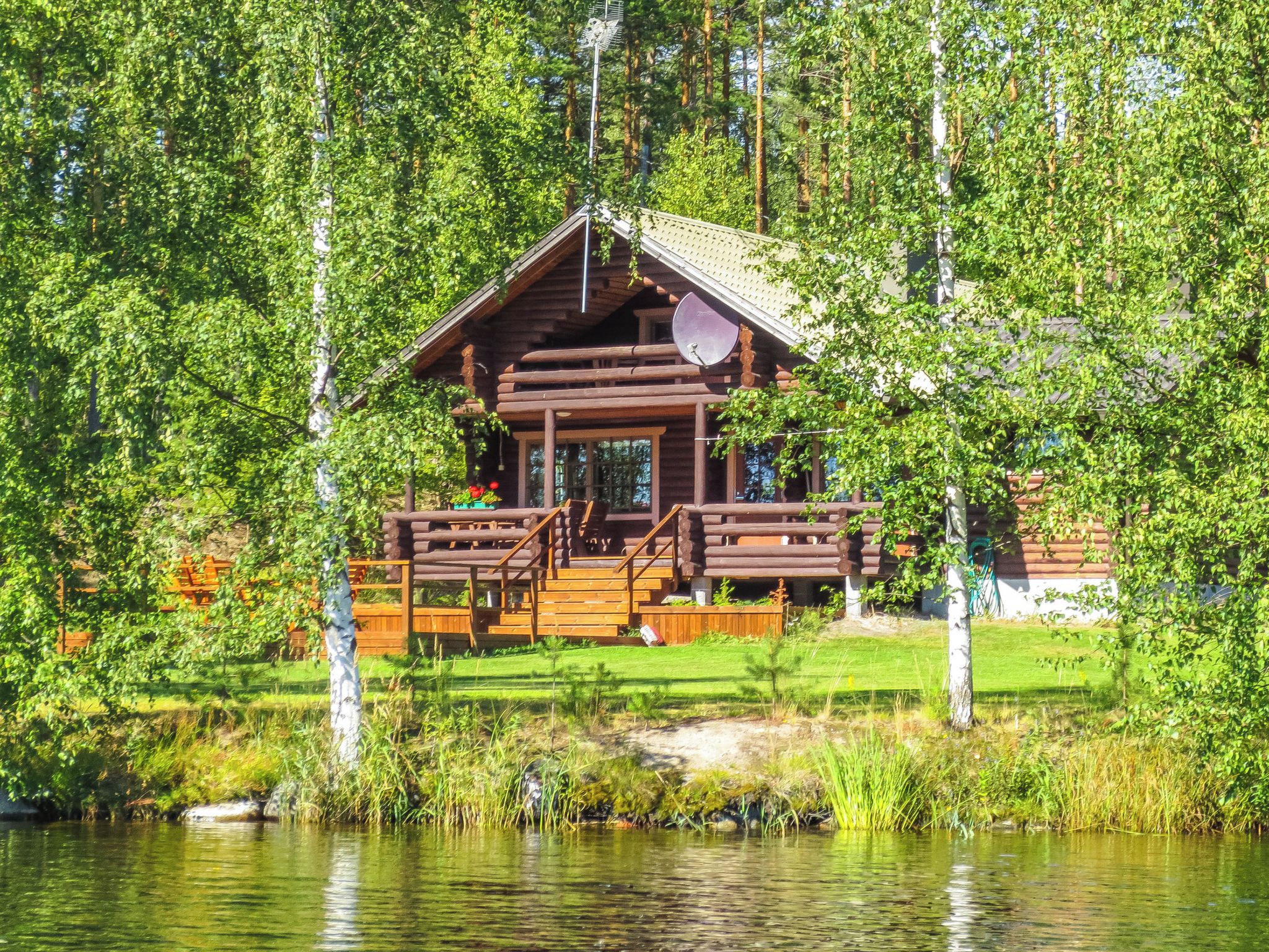 Une cabane en bois dotée d’une terrasse, entourée d’une forêt et d’un lac.