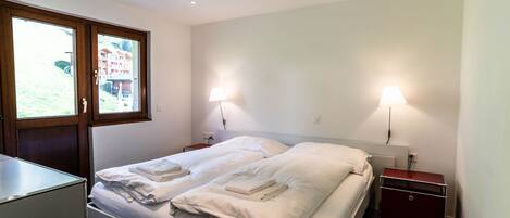 A modern hotel room with a bed, bedside lamps, a desk, and a view through a window.