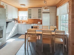 A modern kitchen with white cabinets, a dining table with chairs, and a view of the outdoors through large windows.