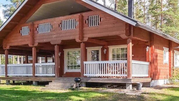 Eine zweistöckige Blockhütte mit Veranda, weißen Geländern und einem Schornstein.