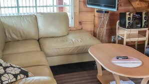 Ein gemütliches Wohnzimmer mit einem beigefarbenen Sofa, einem kleinen Tisch, einem Flachbildfernseher und einer Holztreppe im Hintergrund.