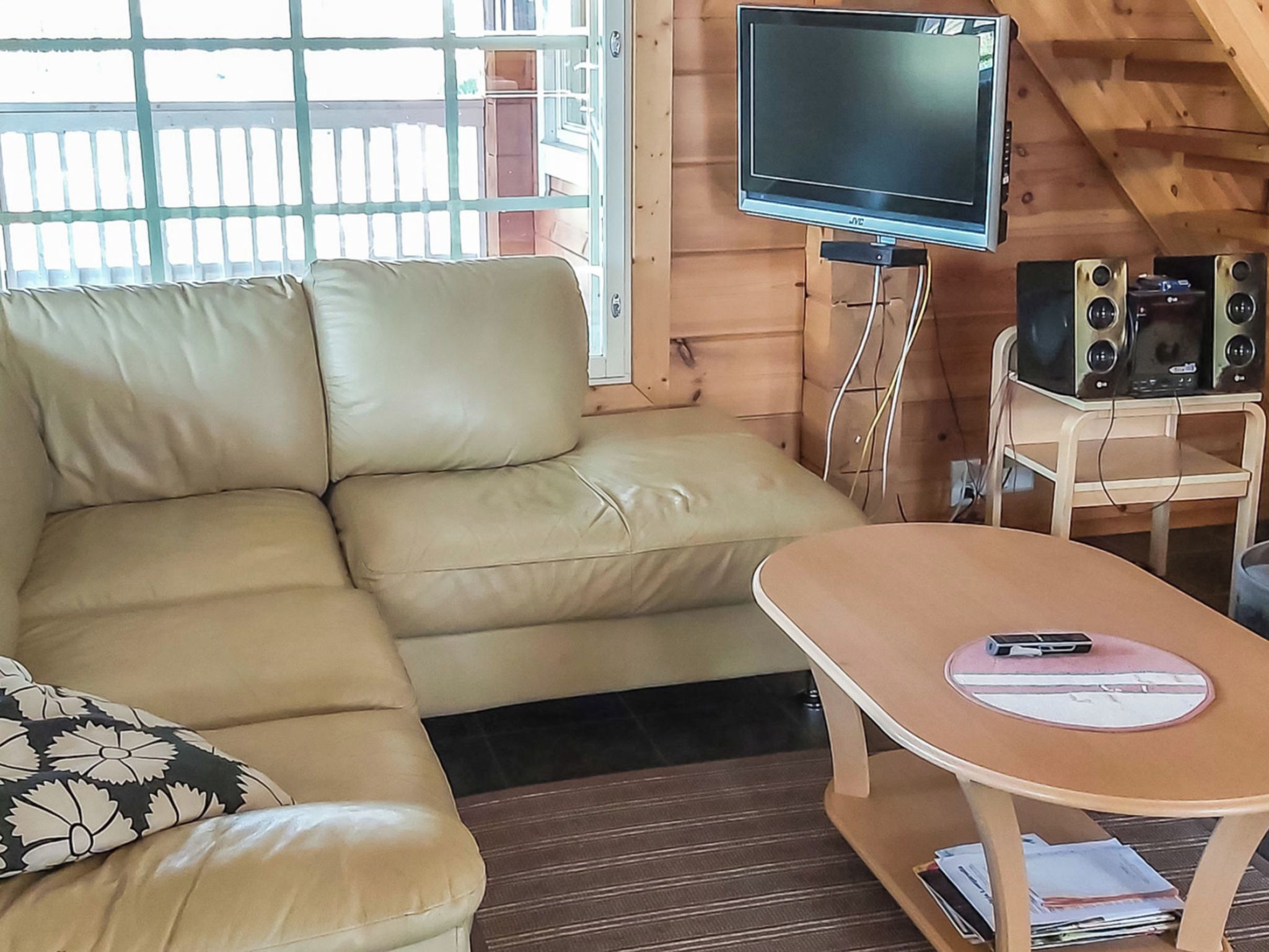 A room with a sofa, a television mounted on a wall, a small table with a mobile phone, and a speaker system.