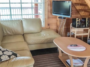 Een kamer met een bank, een aan de muur bevestigde televisie, een tafeltje met een mobiele telefoon en een speakersysteem.