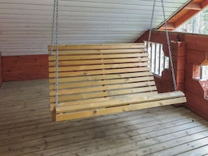 Een houten schommel, opgehangen aan kettingen, in een kamer met houten wanden en vloer.