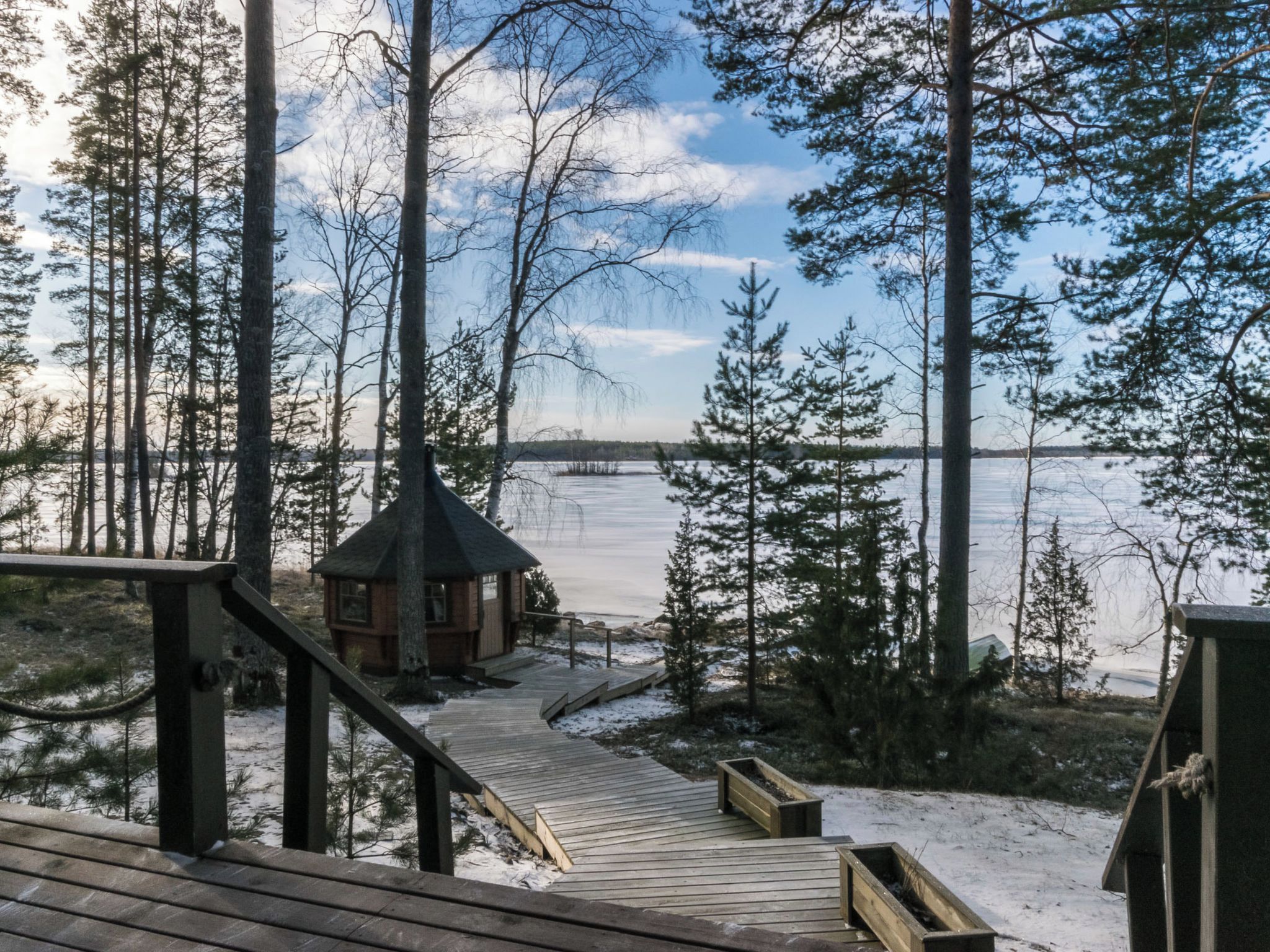 Puinen terassi, joka johtaa mökille, josta on näkymä järvelle ja ympäröiville puille.