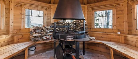 Ein Holzblockhaus-Innenraum mit Holzofen, Bänken und einem Holzstoß.