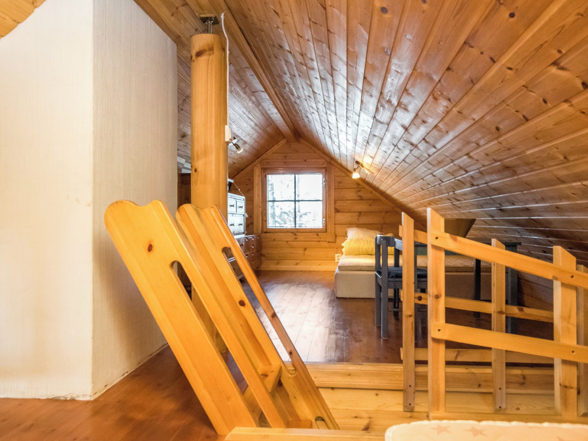 A wooden interior with a sloped ceiling, a window, and a sofa.