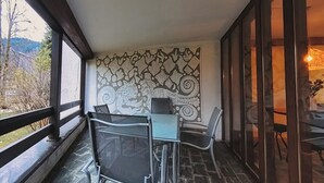 Un balcón con mesa y sillas, un muro con diseño y vistas al exterior.