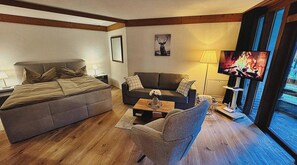 Un salon moderne comprenant un lit, un canapé et un fauteuil, un téléviseur à écran plat et une cheminée.