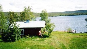 A small cabin with a metal roof, surrounded by lush greenery and a lake. - Raanumökki 1 by Interhome (Pello)