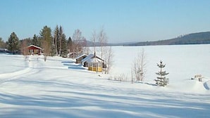 A snow-covered landscape with a wooden cabin and a small building along a clear path. - Raanumökki 1 by Interhome (Pello)