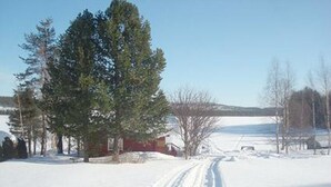 A snowy landscape with a clear sky, a red building, and a large evergreen tree. - Raanumökki 1 by Interhome (Pello)