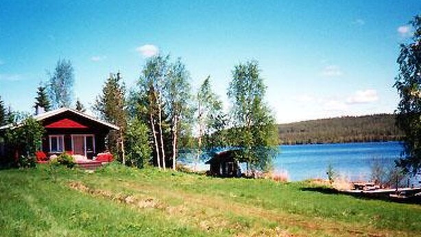 A house with a red roof and a small porch, surrounded by trees and a lake. - Raanumökki 1 by Interhome (Pello)