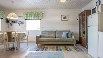 A cozy living room with a sofa, a dining table with chairs, a kitchen area with a refrigerator, and a ceiling fan.