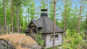 Een klein houten vakantiehuisje in een bos, met een zeshoekig raam en een schoorsteen.