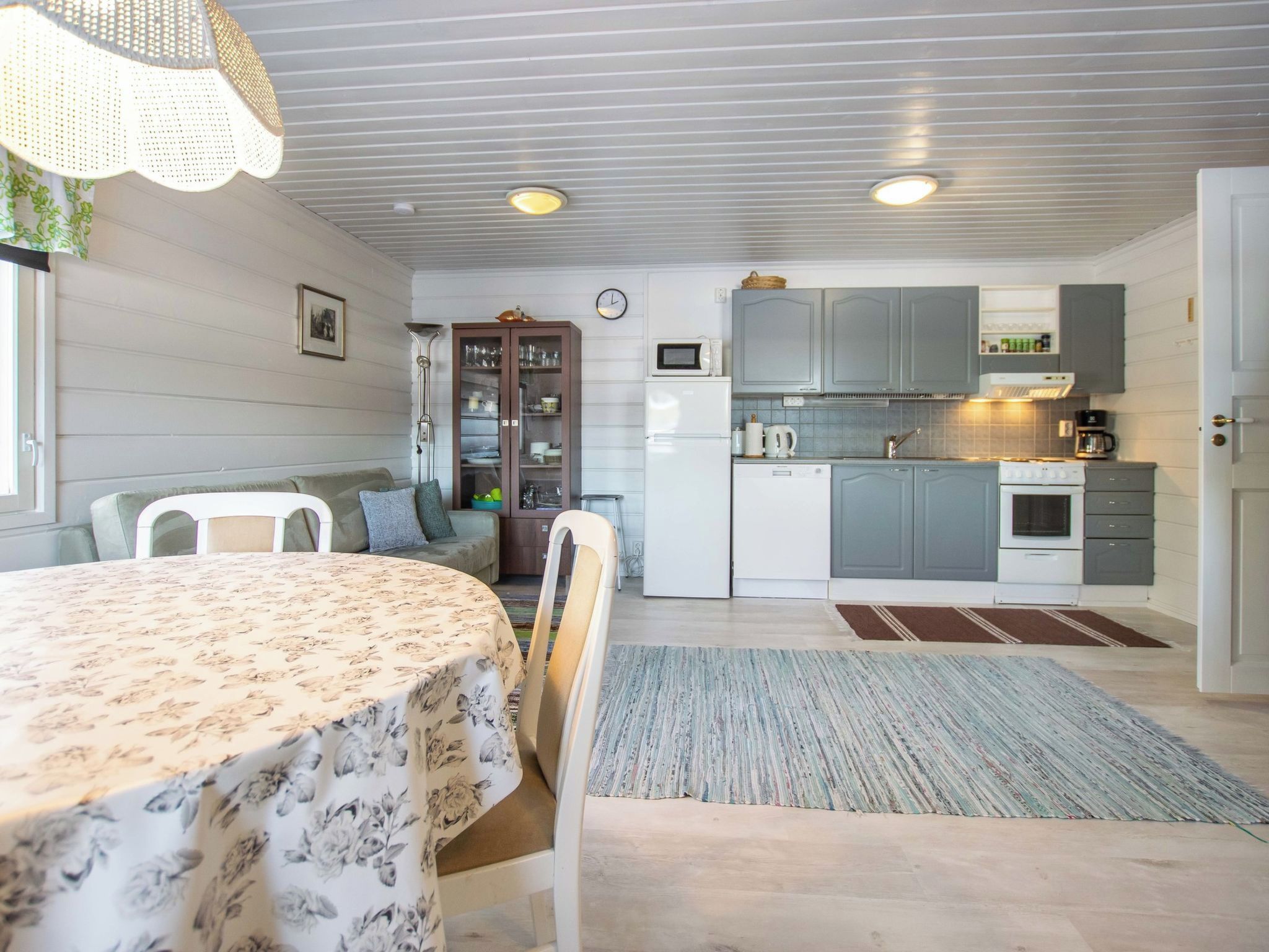Une cuisine compacte dotée d’appareils électroménagers modernes, un coin repas avec une table et des chaises, et un espace de vie comprenant un canapé et une lampe.