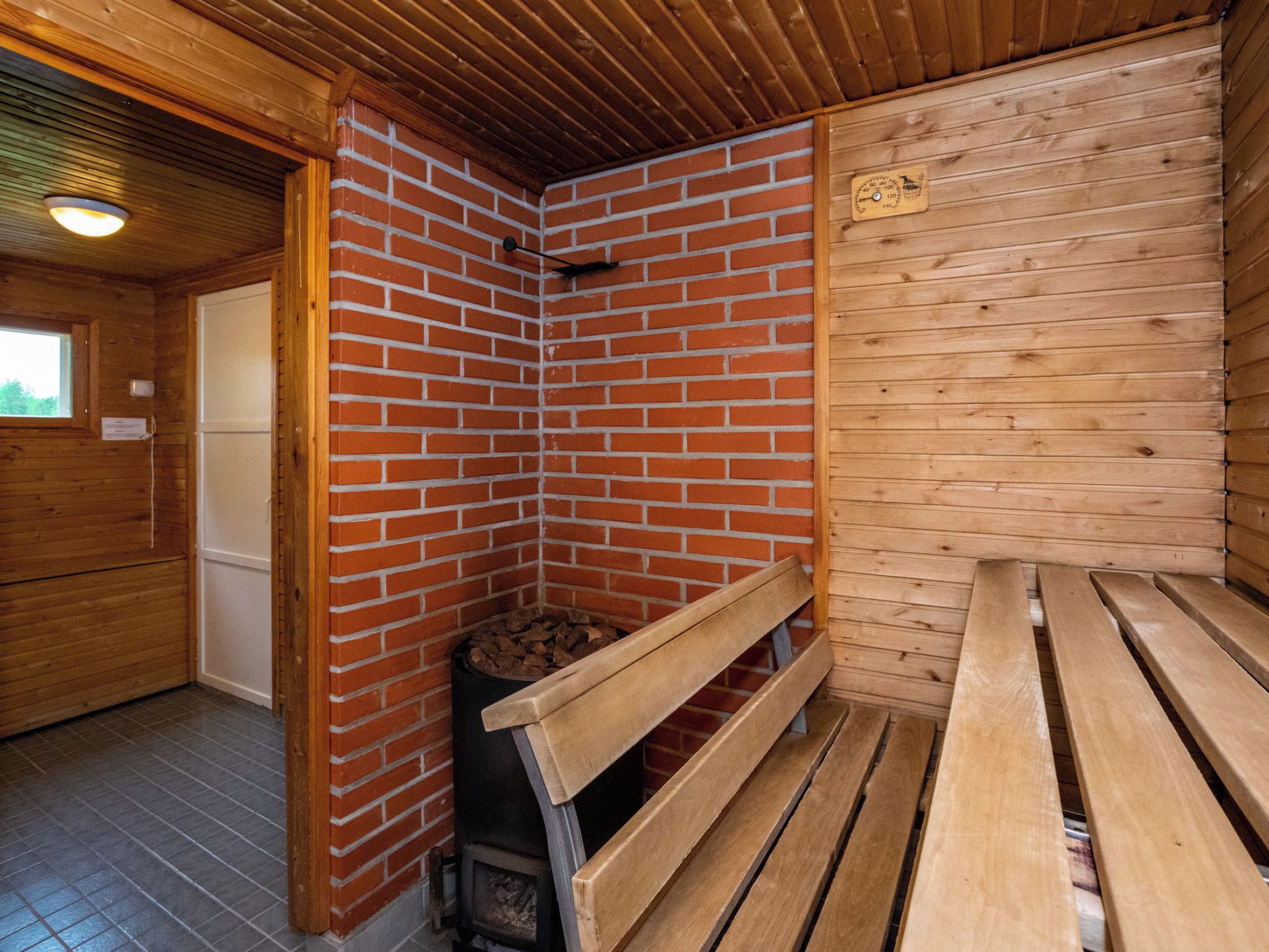 A sauna room with a brick wall, wooden benches, a bench with a backrest, and a wooden ceiling.