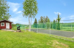 Una cancha de tenis con red, un pequeño edificio rojo y una estatua de lobo.