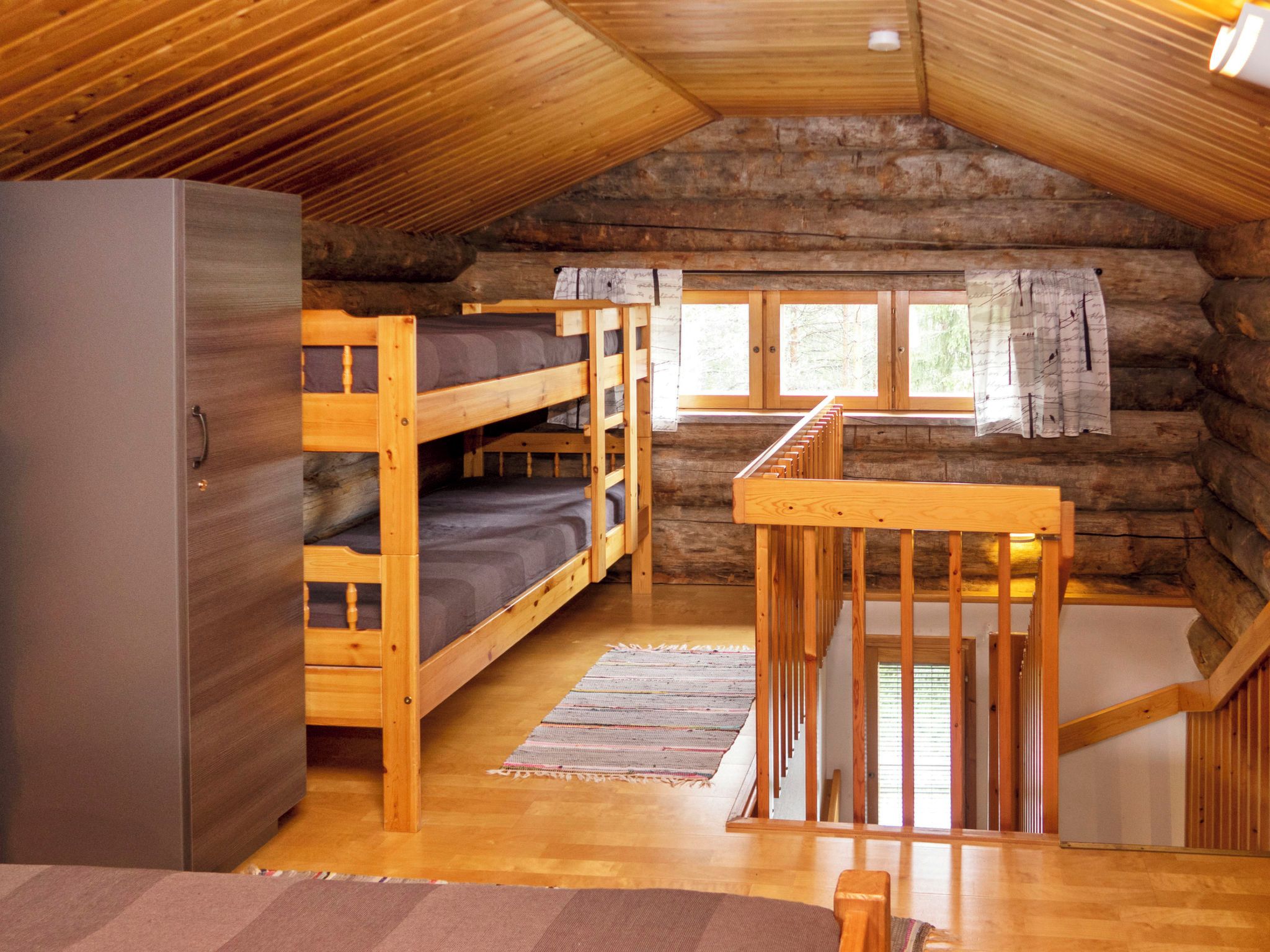 Une cabine avec des lits superposés, un escalier en bois et une grande fenêtre.