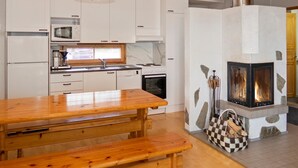 A kitchen with white cabinets, a wooden table, and a stone fireplace with a checkered basket of wood.