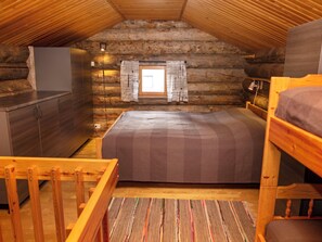 A log cabin bedroom with a bunk bed, a small window with curtains, and a wooden dresser.
