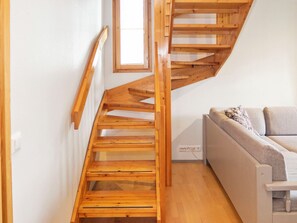 A wooden staircase leading to an upper floor, a sofa with patterned cushions, and a window providing natural light.