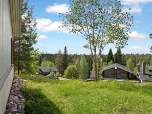 A cabin with a stone foundation, surrounded by a grassy area and trees, with a forest in the background.