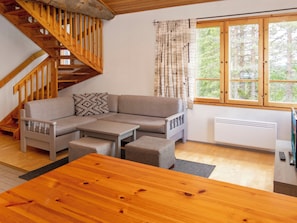 A modern living room with a wooden staircase, a sofa set, a coffee table, and a large window with a view of trees.