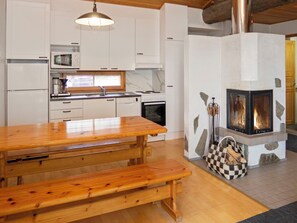 A kitchen with white cabinets, a wooden table, and a stone fireplace with logs.