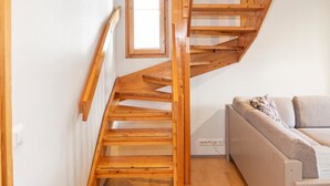 A wooden staircase with a simple design, leading to a living area with a sofa and a small table.