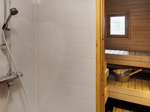 A bathroom with white tiles, a shower, and a wooden sauna area with a window.