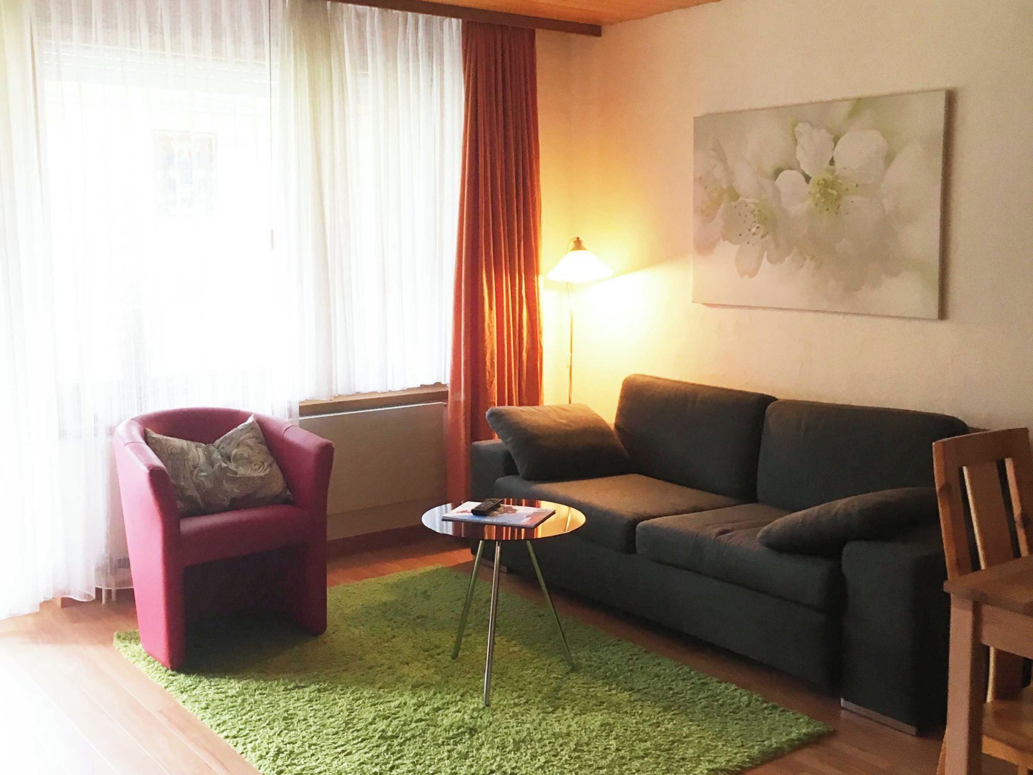 Ein Wohnzimmer mit einem roten Sessel, einem grauen Sofa, einem kleinen runden Tisch und einer Lampe.