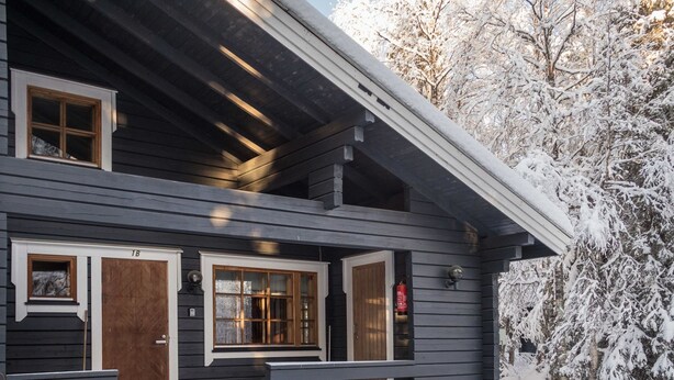 A two-story log cabin with a front porch, wooden doors, and windows.