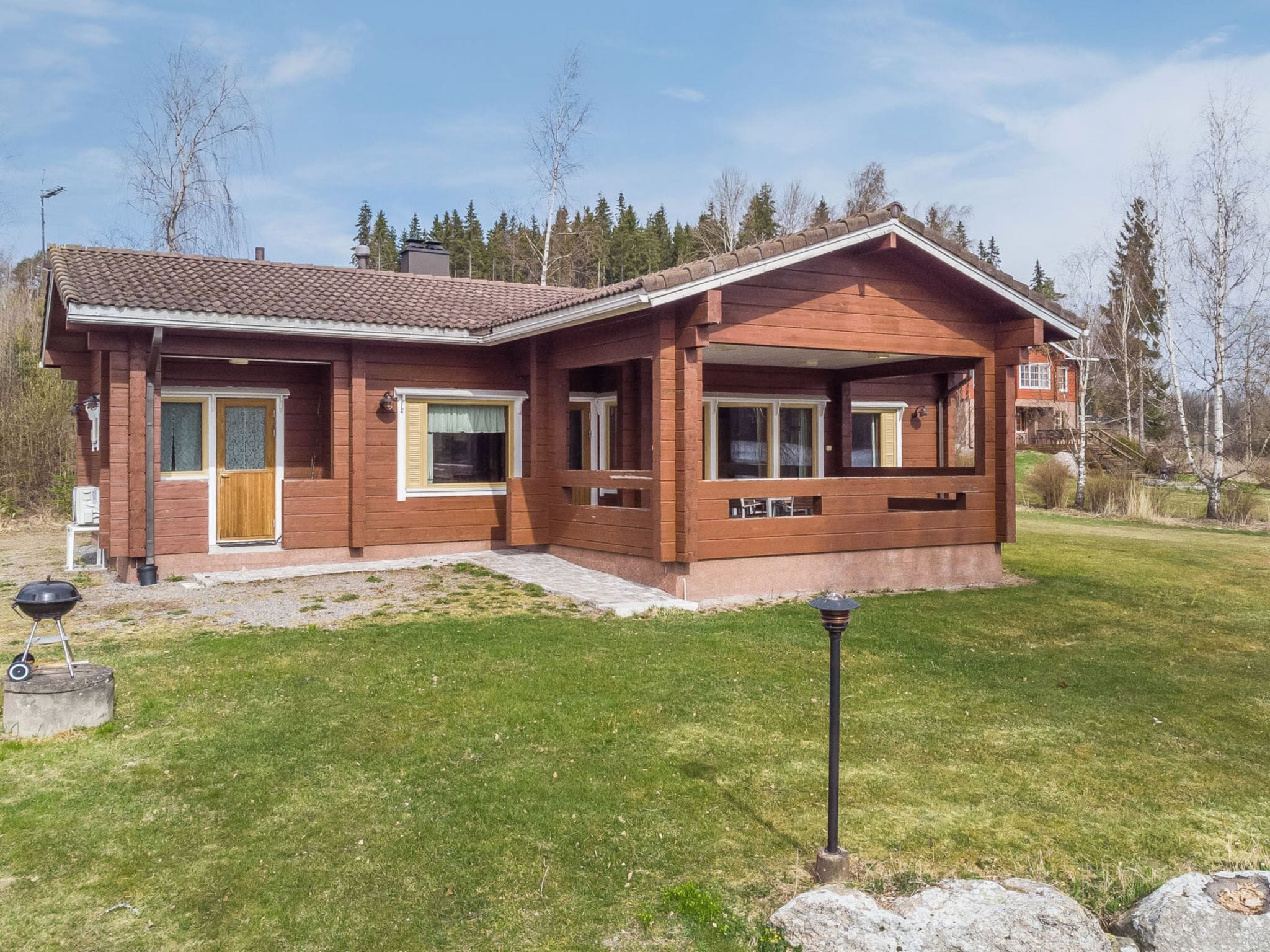 Une maison en bois à deux étages, dotée d’un porche à l’avant, d’une cheminée et d’une pelouse bien entretenue.